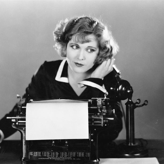 Black and white vintage photo of a woman on a telephone sitting in front of a typewriter